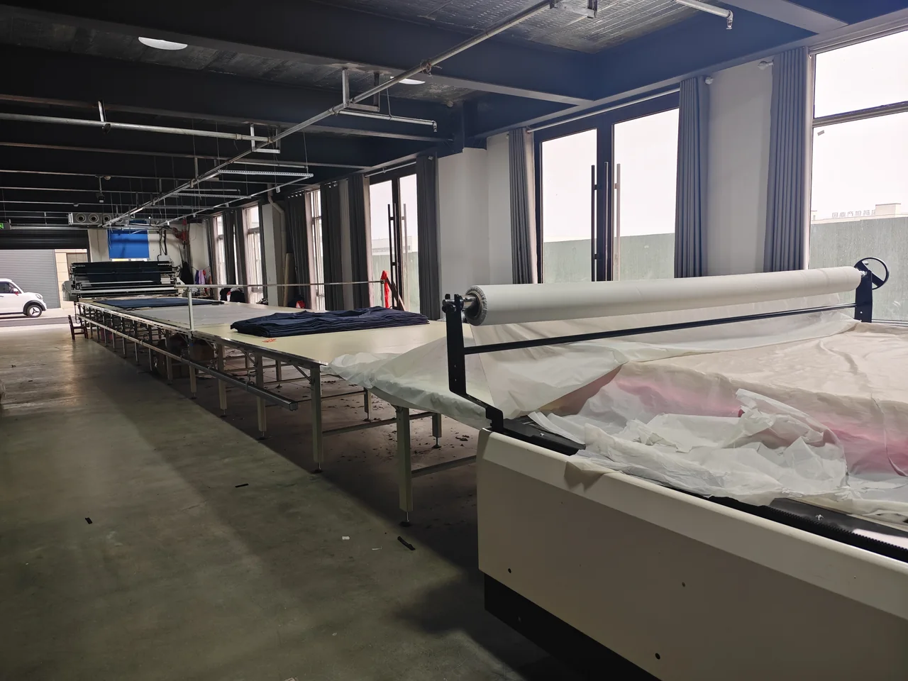 Long fabric spreading table with rolls and cutting equipment inside the workshop